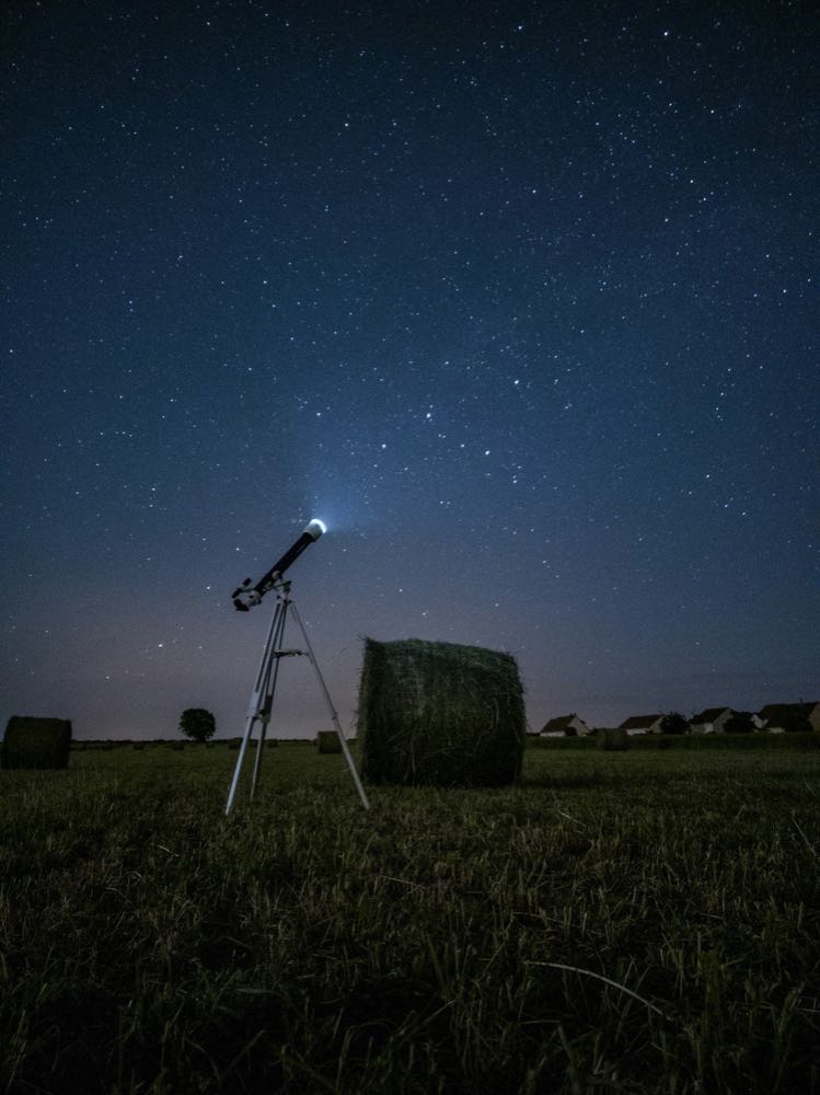 A small telescope pointed at a star-filled night sky over a field.